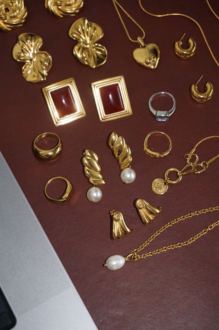 Collection of gold jewelry including rings, earrings, and necklaces on a brown surface. Highlighting Wing Earrings.