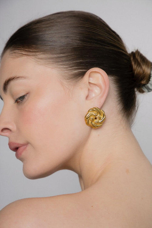 Woman wearing a gold knot earring against a neutral background