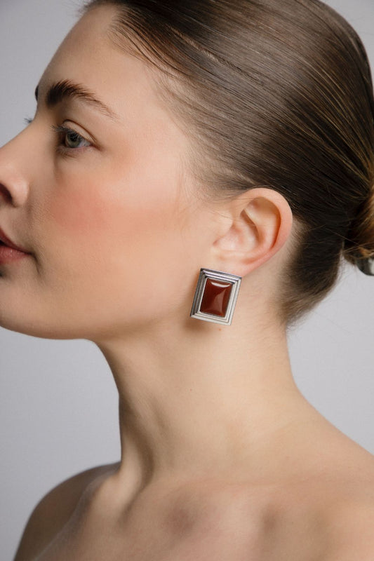 Close-up of a woman wearing a square earring with a red gemstone on a neutral background
