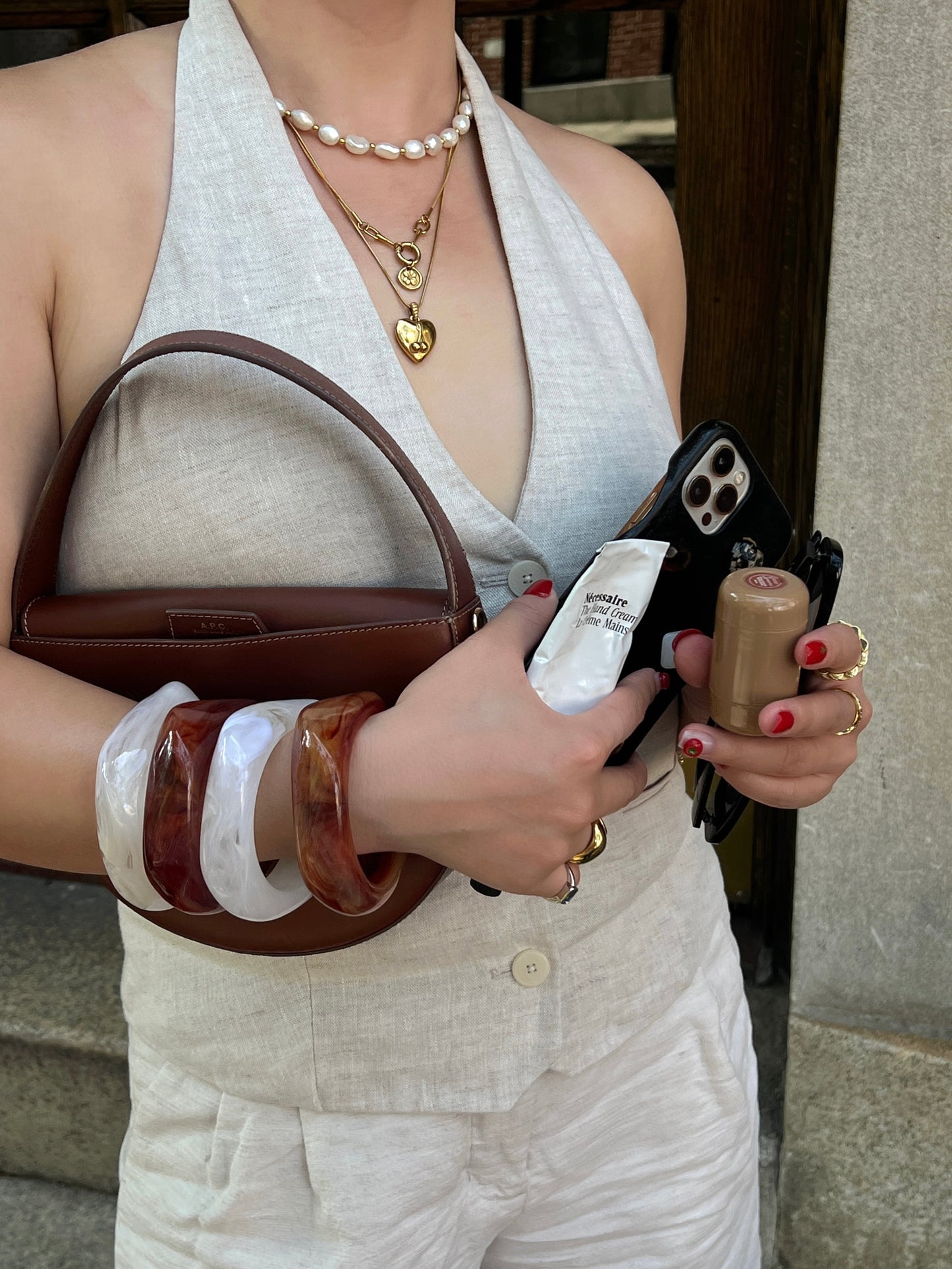 Person holding a brown handbag, phone, and wearing 4 bangles