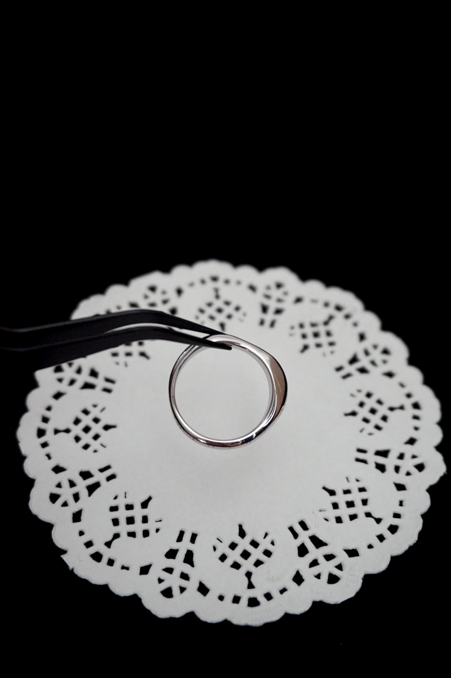 Minimal silver ring on a white doily against a black background