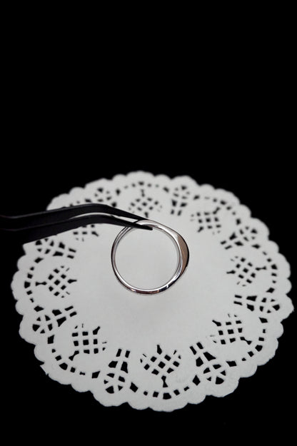 Minimal silver ring on a white doily against a black background