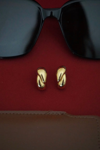 Gold earrings on a red surface with black sunglasses in the background