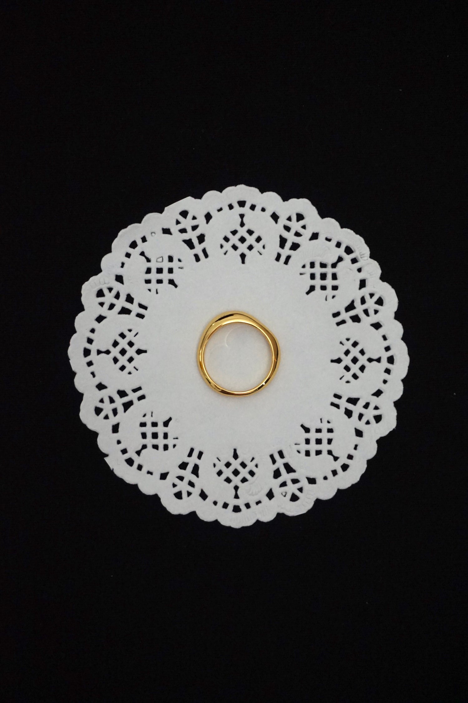Minimal gold ring on a white doily against a black background