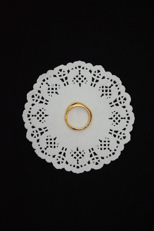 Minimal gold ring on a white doily against a black background