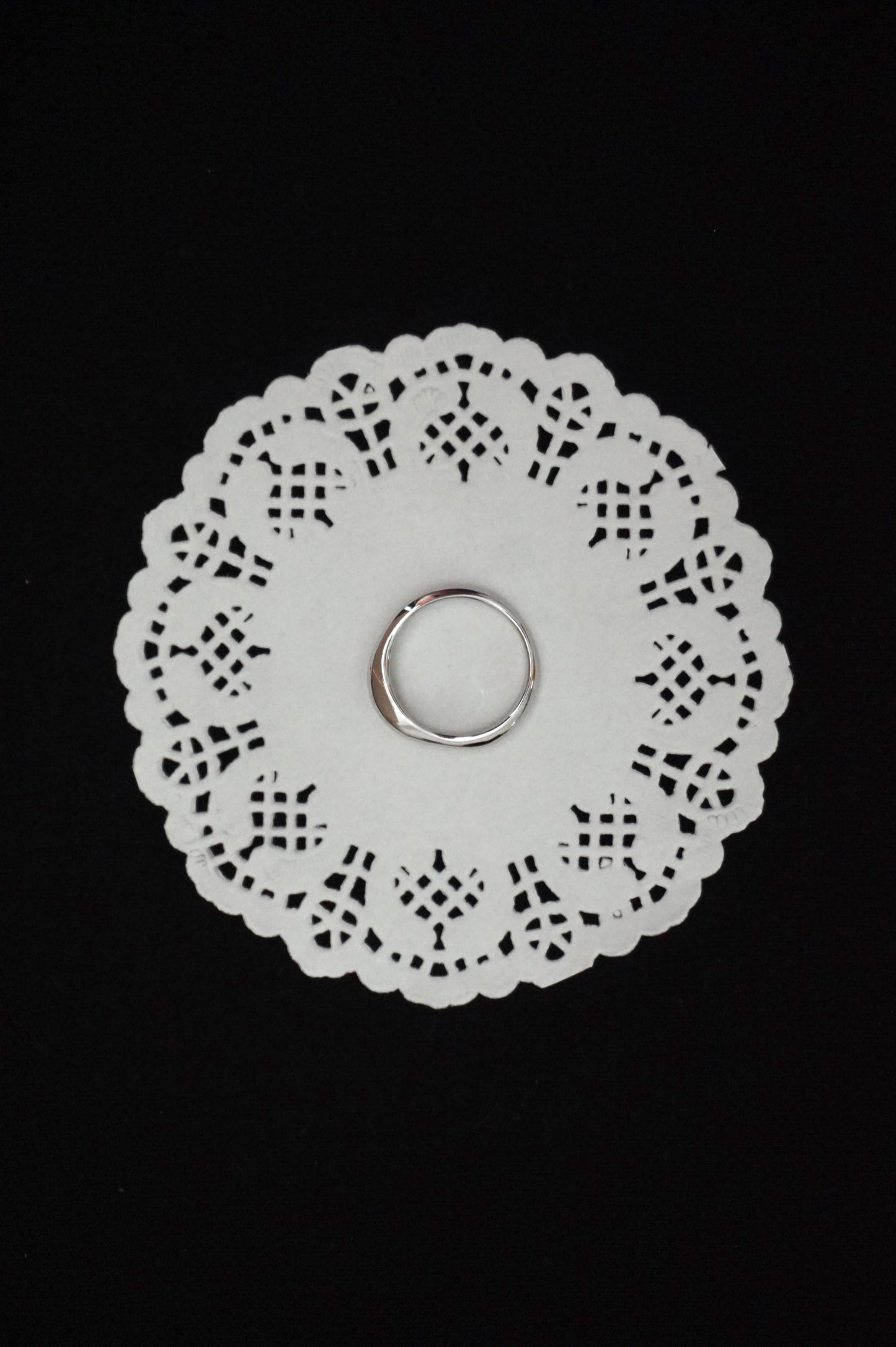 White paper doily with a minimal silver ring on a black background