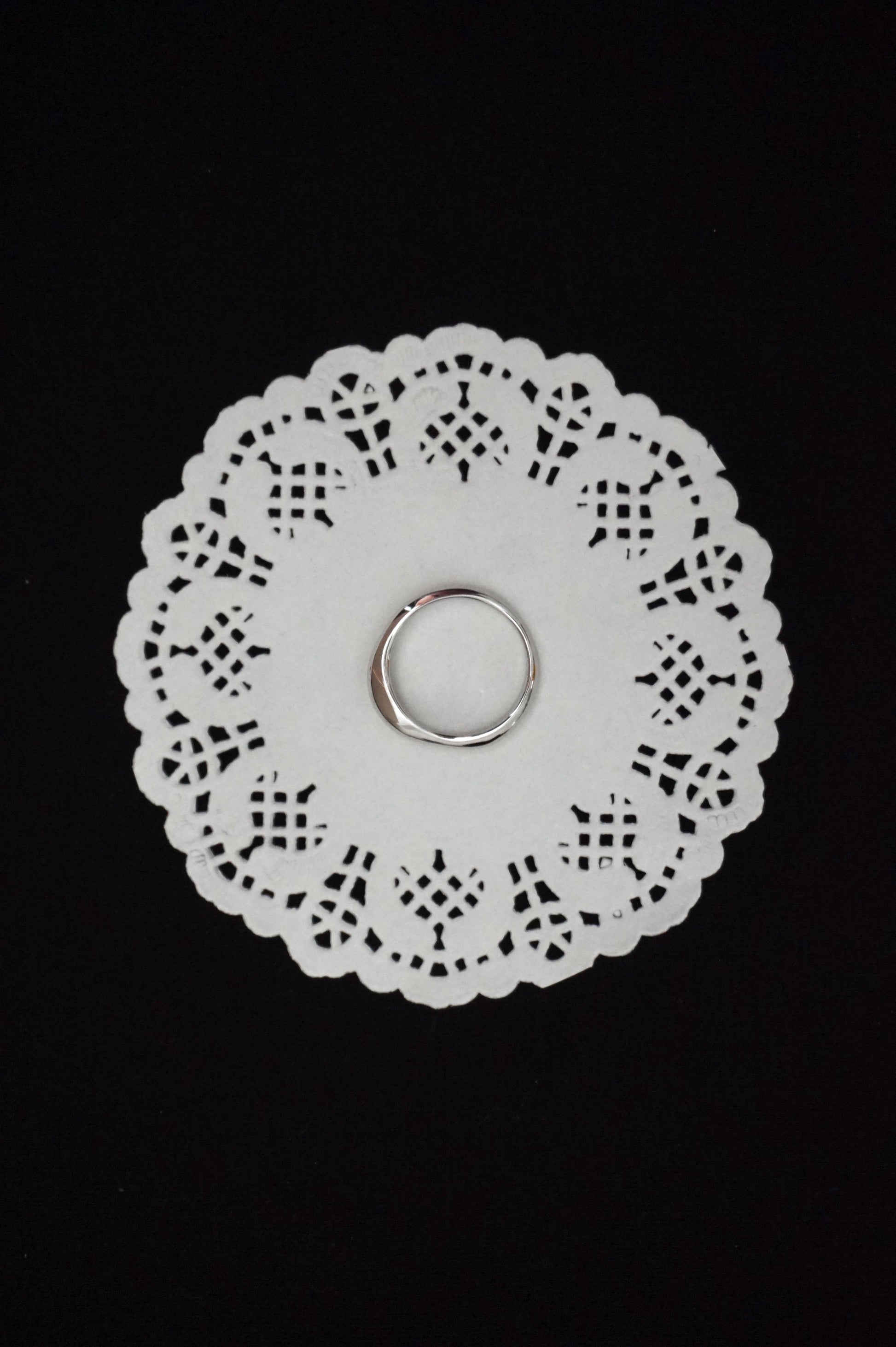 White paper doily with a minimal silver ring on a black background