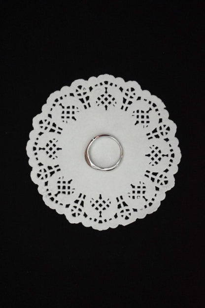 White paper doily with a minimal silver ring on a black background
