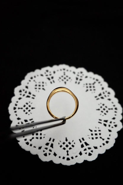minimal everyday gold ring on a white doily with tweezers against a black background
