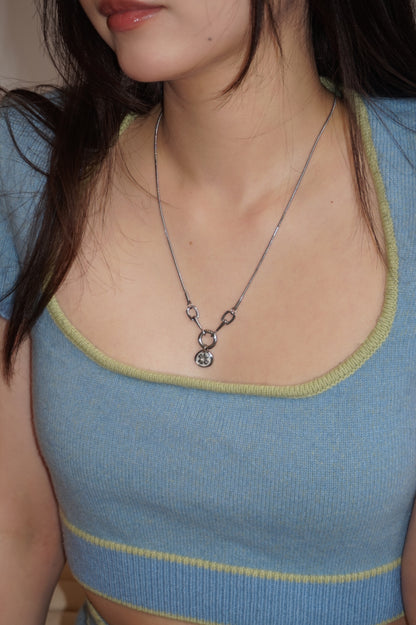A model wearing blue sweater with a square neckline, showcasing Lucky Charm Necklace in silver