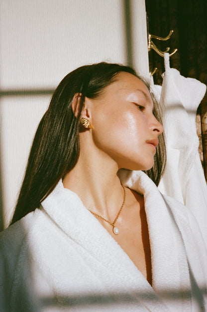 a model wearing shell earrings and pearl pendant necklace on a robe