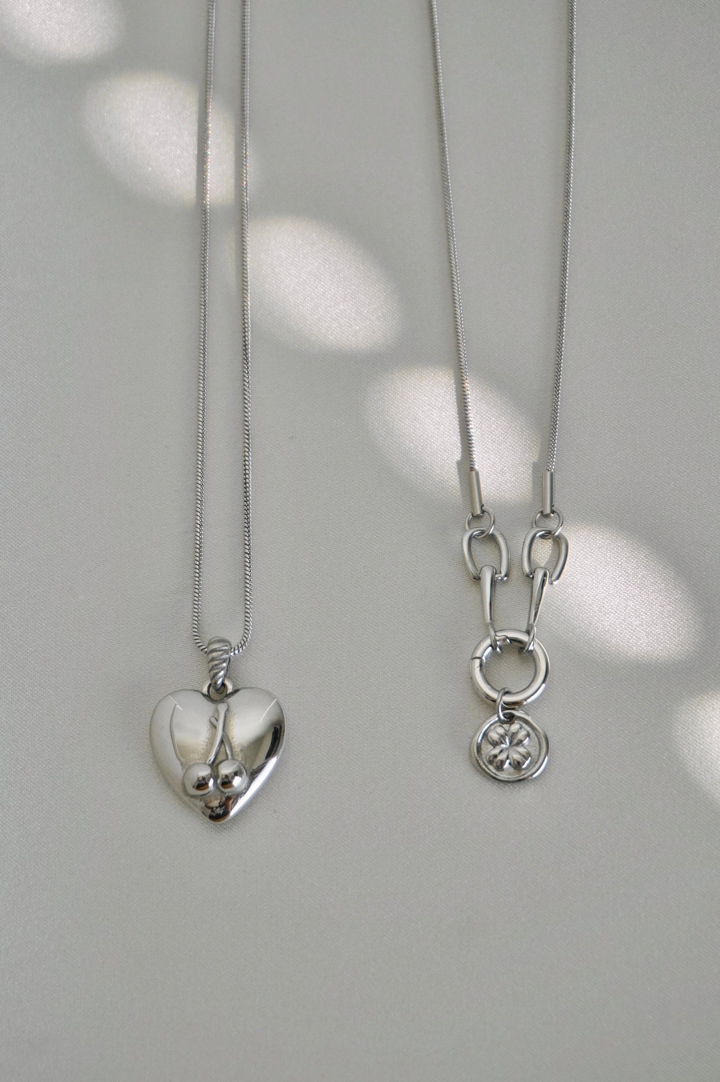 Lucky charm necklace and Cherry Heart necklace laying side by side on a white background