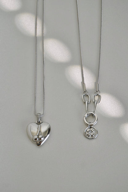 Lucky charm necklace and Cherry Heart necklace laying side by side on a white background