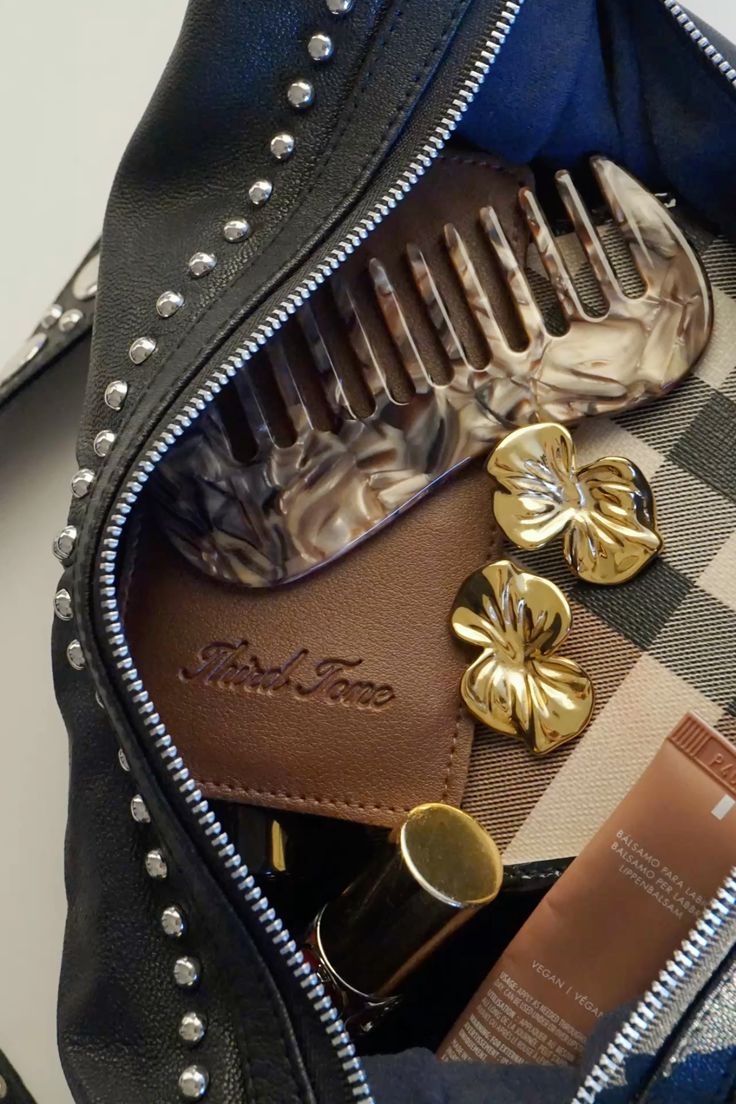 Third Tone Mocha Comb placed inside a black studded bag with Orchid Earrings alongside with other everyday essential items.